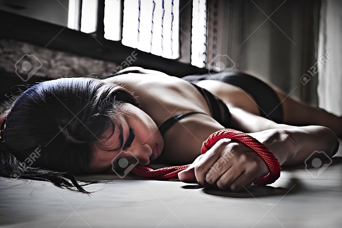Porträt. Frau liegt auf dem Boden, nachdem sie festgenommen und vergewaltigt wurde. In ihrer Hand war ein rotes Seil gebunden. Und sie hält das Kondom. Kondome sind in funktionstüchtigem Zustand. Gewaltsame Empfängnis. EIN