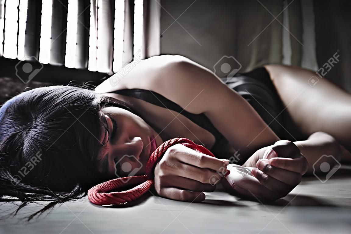Porträt. Frau liegt auf dem Boden, nachdem sie festgenommen und vergewaltigt wurde. In ihrer Hand war ein rotes Seil gebunden. Und sie hält das Kondom. Kondome sind in funktionstüchtigem Zustand. Gewaltsame Empfängnis. EIN