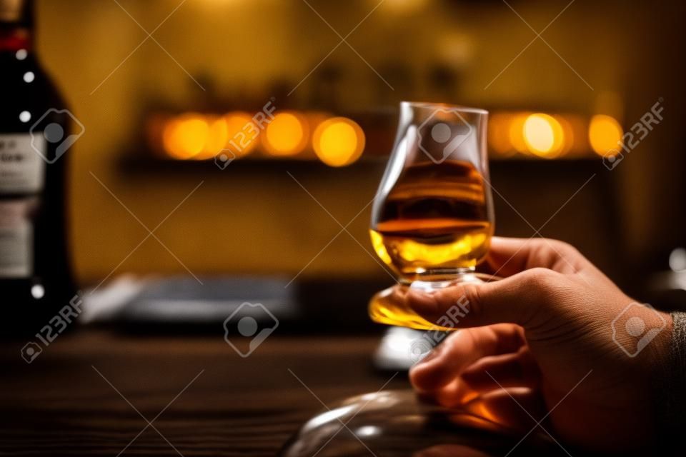 Bliska strzał dłoni trzymającej szklankę whisky Glencairn single malt.