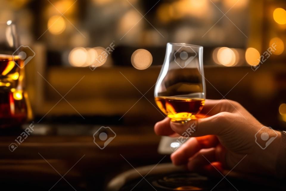 Bliska strzał dłoni trzymającej szklankę whisky Glencairn single malt.