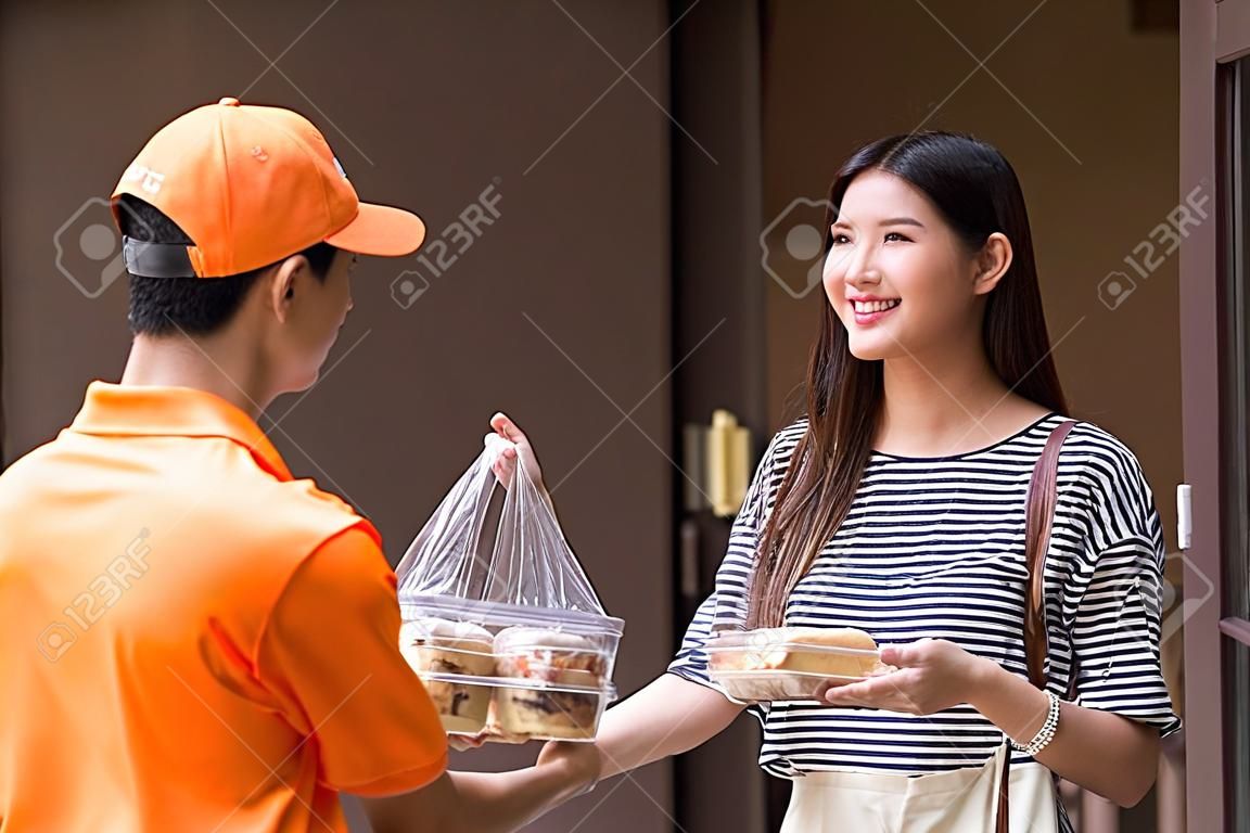 livreur en uniforme orange donnant une boulangerie de pain à une cliente souriante devant un appartement ou un condo. Nouvelle norme pour commander de la nourriture en ligne pendant la pandémie de covid-19.