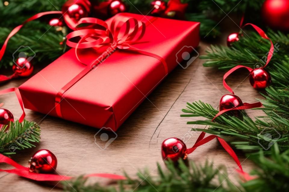 Presente de Natal na placa de madeira com abeto, sinos vermelhos. Fita vermelha na caixa de presente de papel. Vista superior do closeup com espaço da cópia.