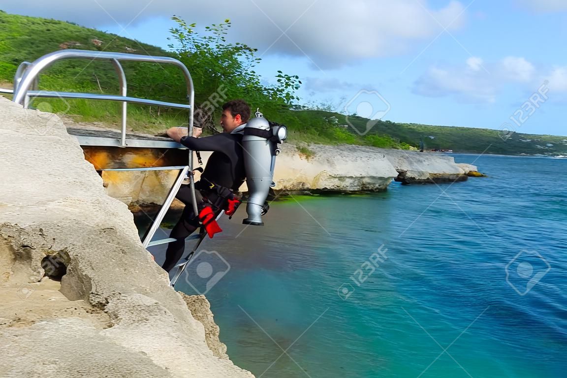 Scuba diver on the steel ladder coming out from the sea. Rocky coastline with scuba diver in diving equipment. Scuba diver on the tropical vacation coming from the water.