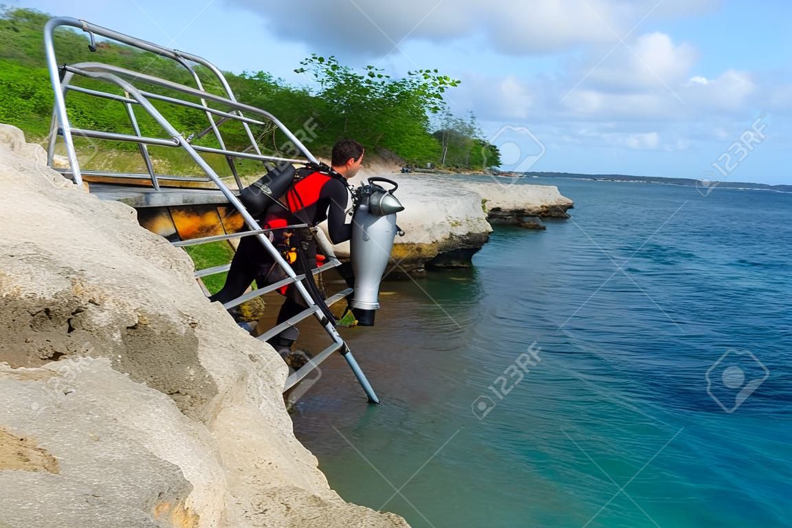 Scuba diver on the steel ladder coming out from the sea. Rocky coastline with scuba diver in diving equipment. Scuba diver on the tropical vacation coming from the water.