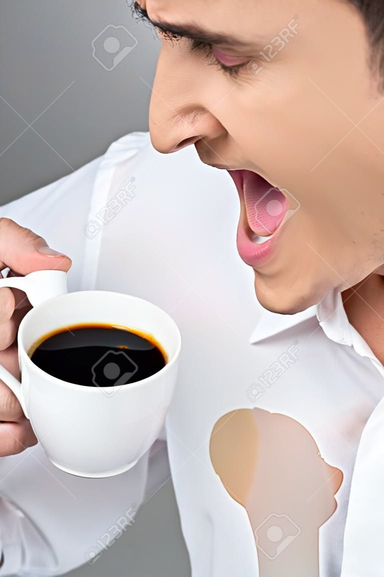 Człowiek jest rozlewając kawę na białej koszuli podczas picia