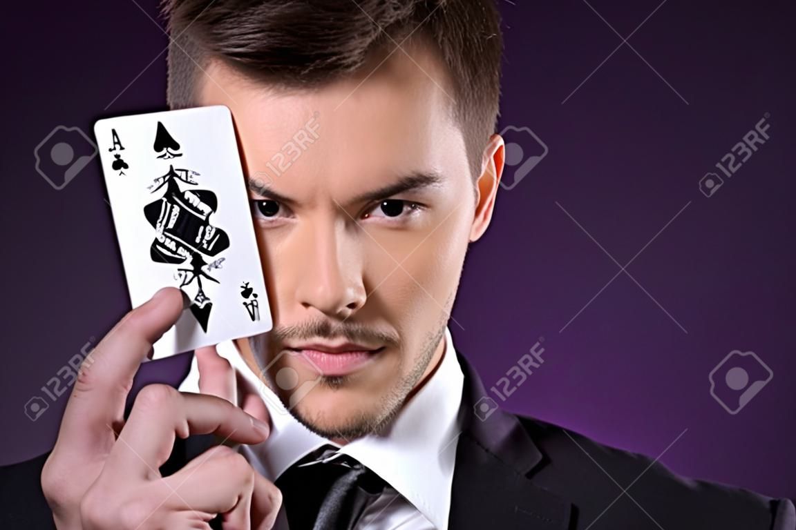 Joker man  Portrait of confident young businessman holding a joker card in front of his eye while isolated on colored background