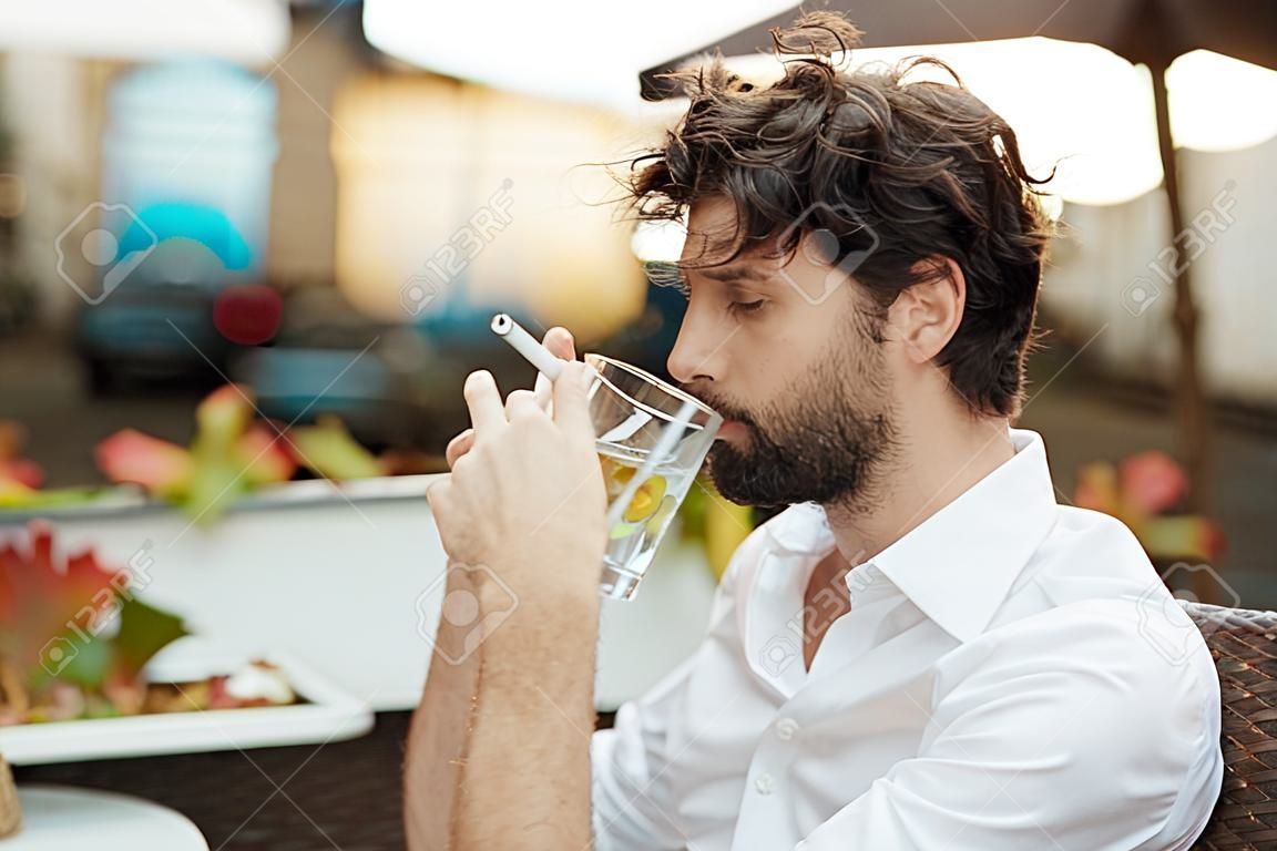 bel homme élégant assis à l'extérieur dans une table de restaurant, travaille et utilise un ordinateur portable tout en fumant des cigarettes