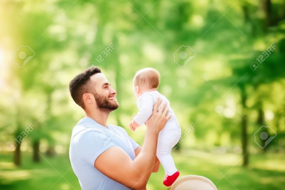 年輕的父親拿著武器的戶外公園微妙的新生嬰兒。快樂育兒的理念，父親節和家人