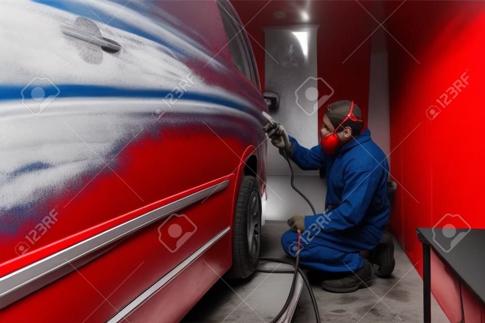 Auto mechanic working in automotive manufacturing industry and painting a red van in a special booth