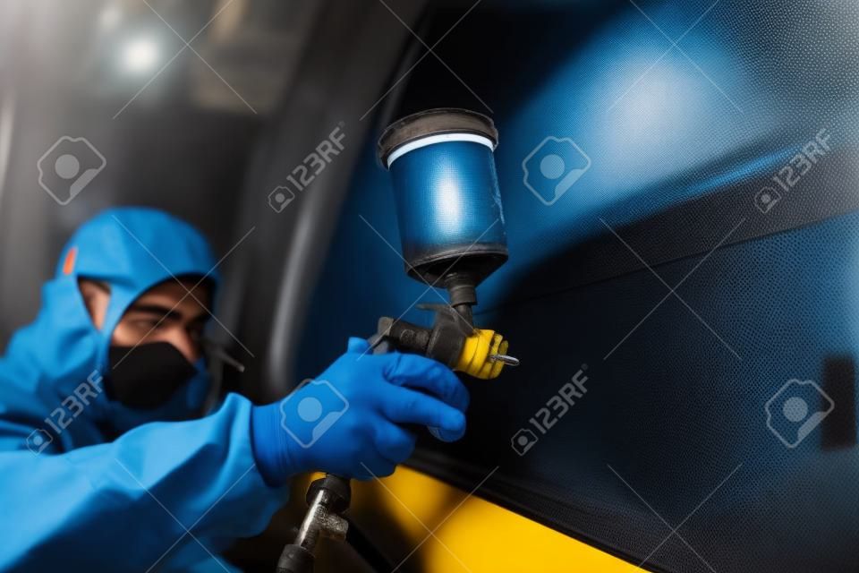mechanic worker painting a car in a special painting box, wearing a full body costume and protection gear