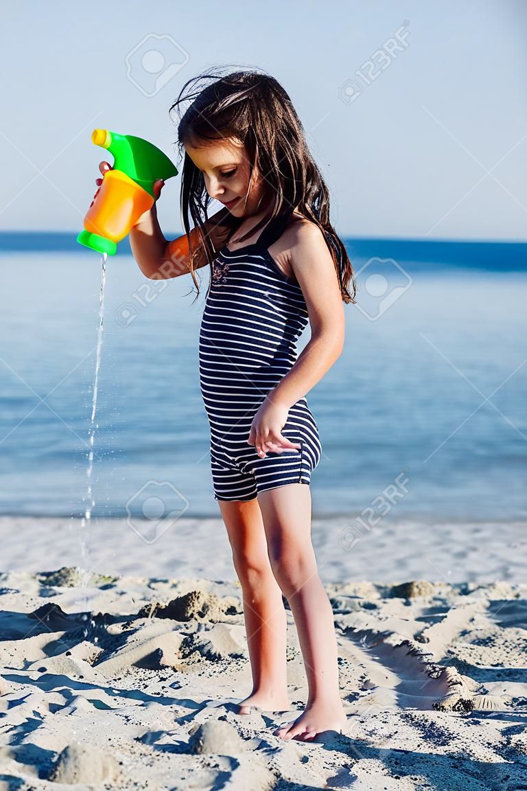 Petite petite fille plaing avec de l'eau sur la plage de sable à l'été