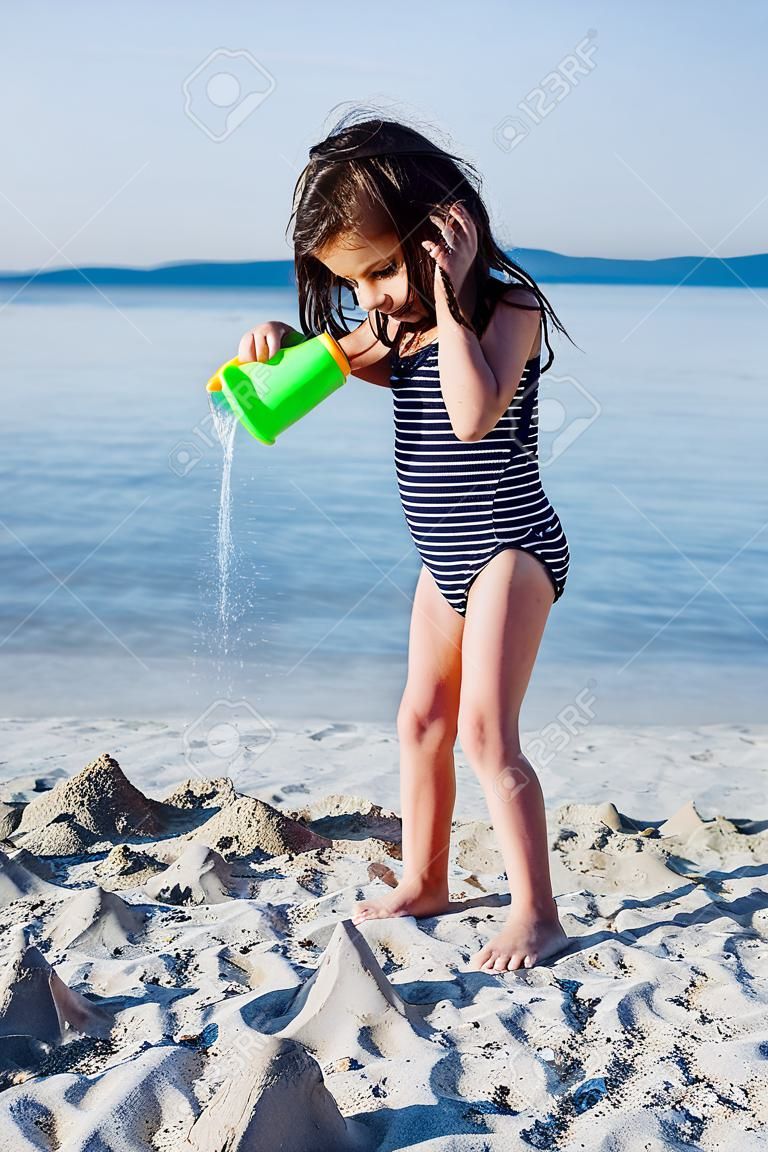 Nettes kleines Mädchen , das mit Wasser am sandigen Strand im Sommer balanciert