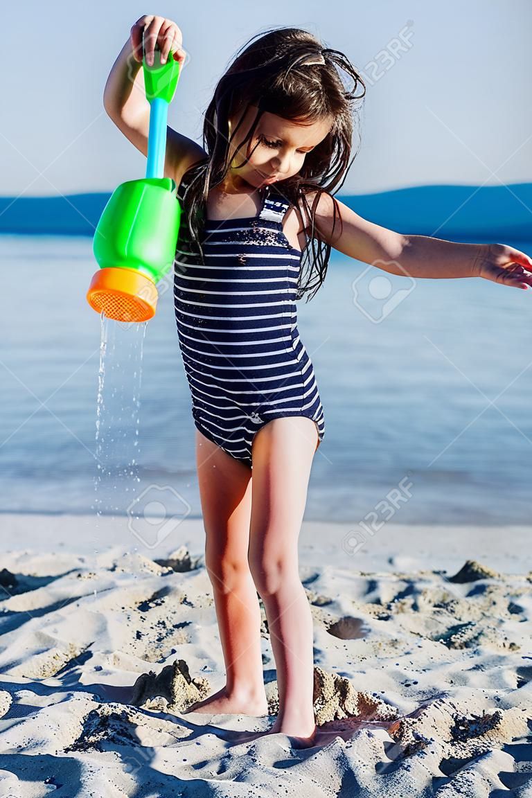 Cute little girl plaing with water on the sandy beach at summer