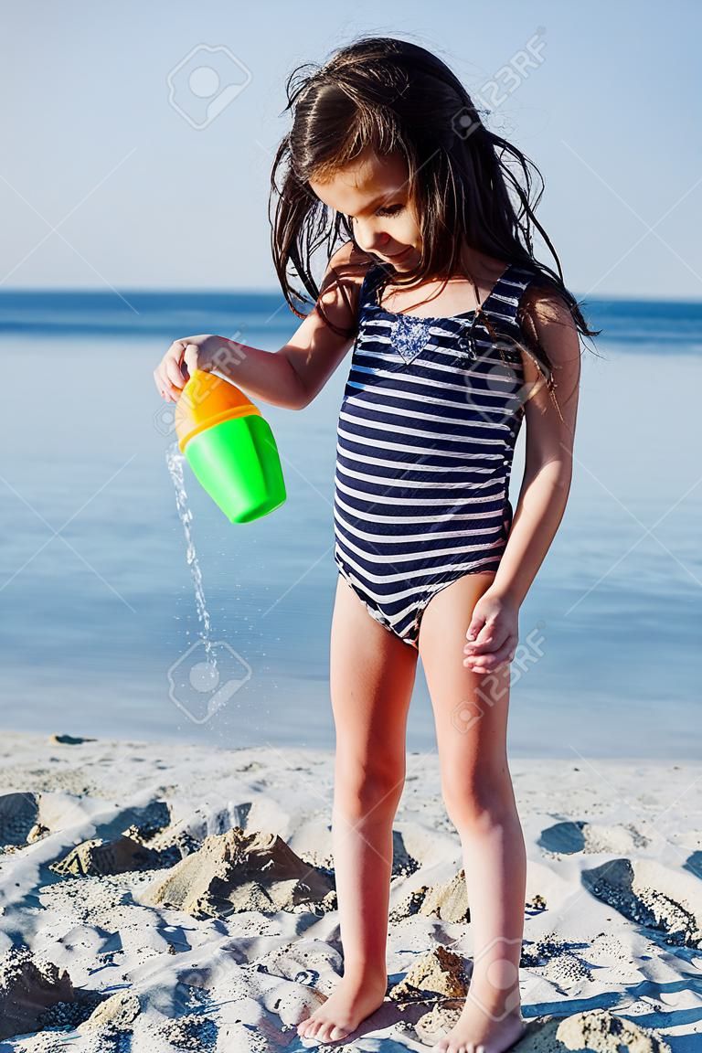 夏の砂浜のビーチの上に水でかわいい小さな女の子 plaing