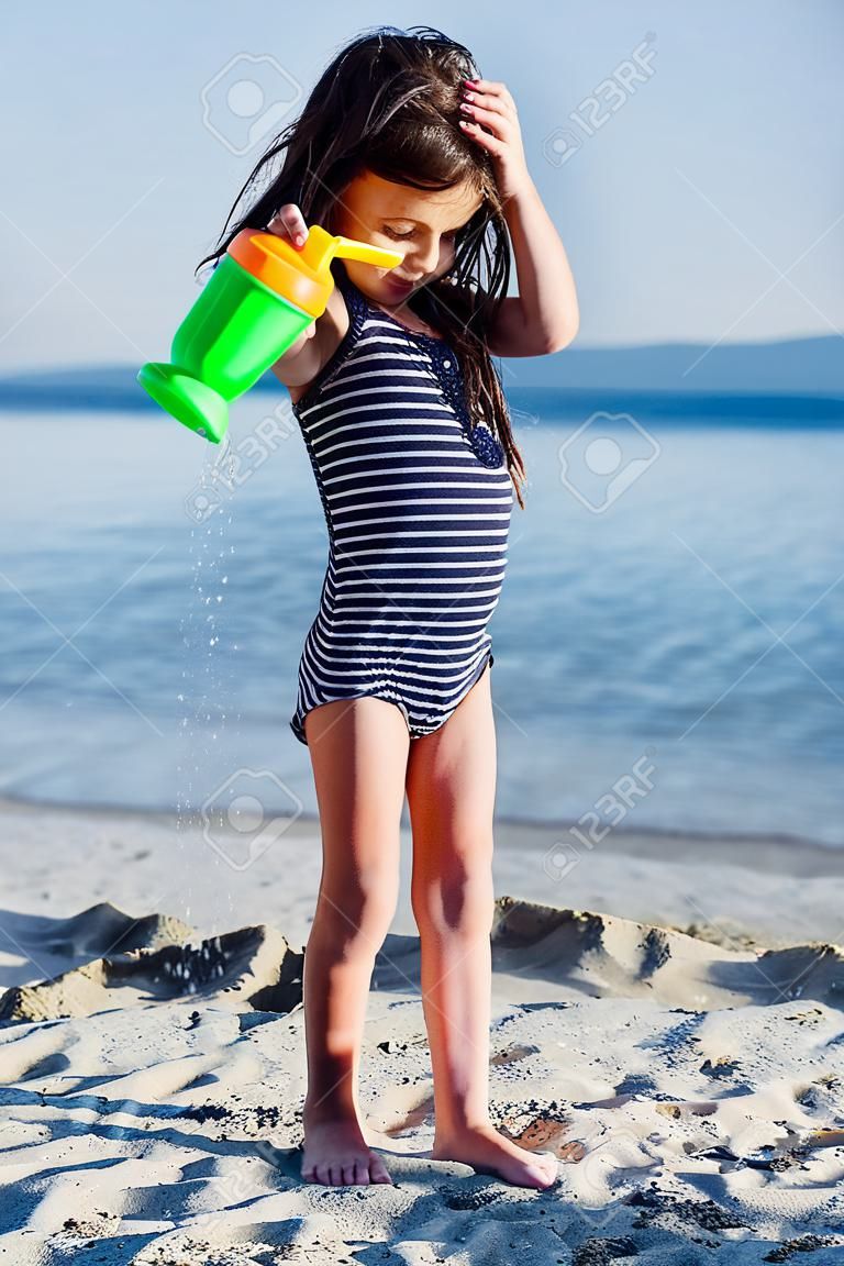 Cute little girl plaing with water on the sandy beach at summer