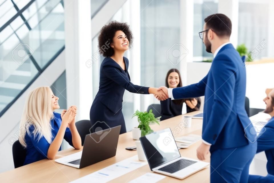 Jonge zakenmensen schudden handen in het kantoor bij het afronden van een succesvolle vergadering
