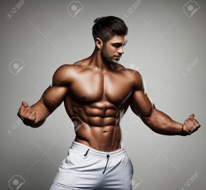 年輕英俊的人肌肉的健美運動員在白色背景上的工作室冒充