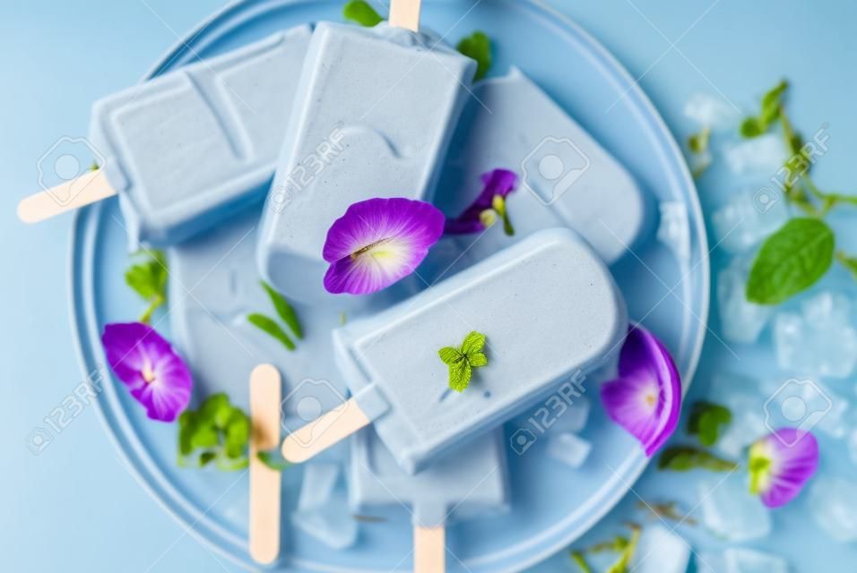 Naturally organic summer sweets, homemade blue and violet ice cream popsicles with butterfly pea flower tea, grey concrete background copy space