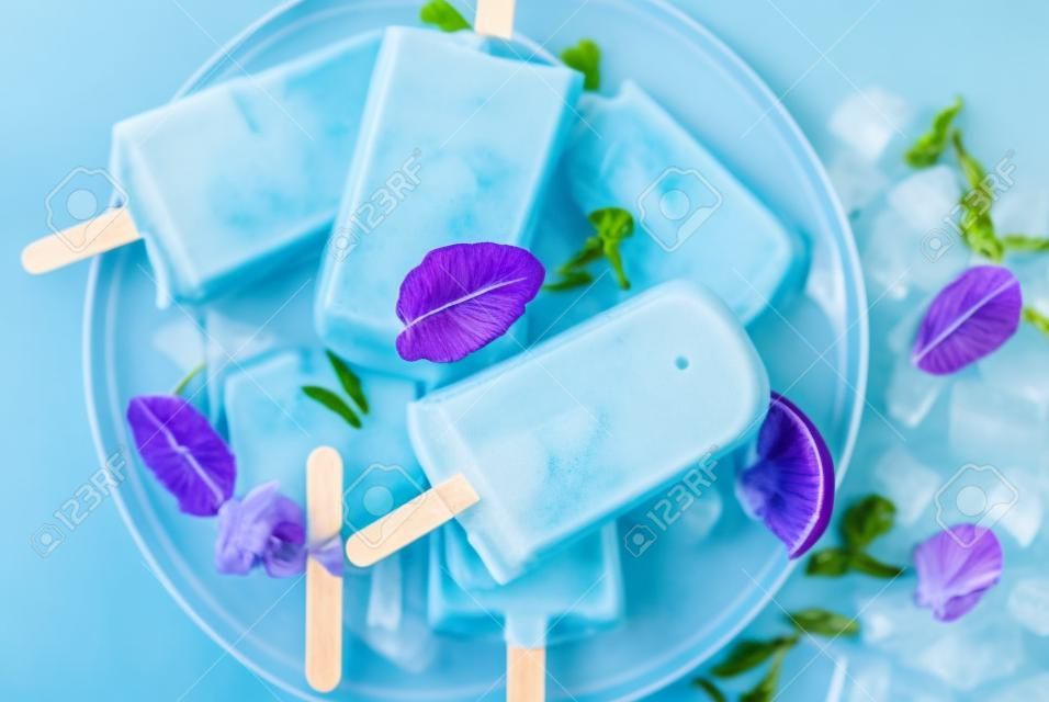 Naturally organic summer sweets, homemade blue and violet ice cream popsicles with butterfly pea flower tea, grey concrete background copy space