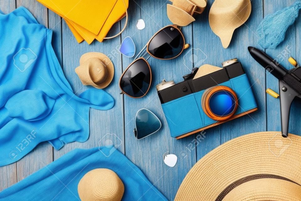 Heldere zomer platte-lay achtergrond. Oude blauwe houten achtergrond met zomer vrouwen kleding, zonnebril, hoed, camera, paspoorten en vakantie tickets