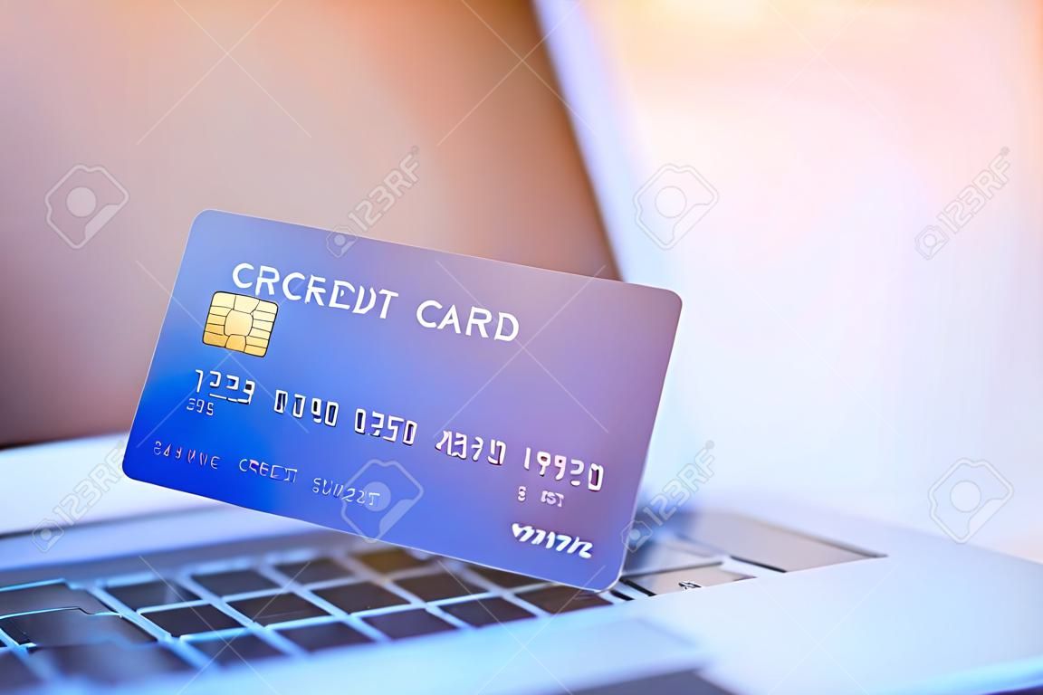 Close-up photo of left hand woman holding blue credit card mockup with a laptop background and copyspace on the right side for text. Easy e-commerce shopping online and payment by credit card