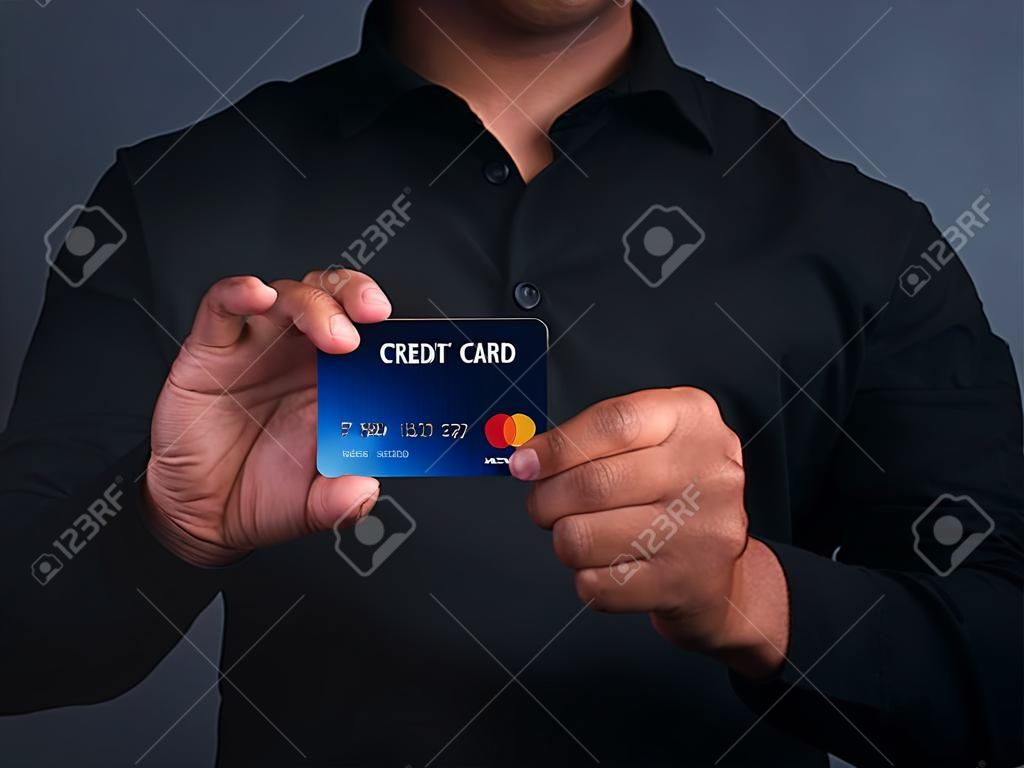 A young man holding a mockup blue credit card and showing thumb up while standing in a studio. Close-up photo. Money and business concept.