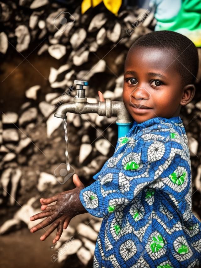 Jeune garçon africain tenant la main sous un robinet. Les problèmes de pénurie d'eau concernent l'accès insuffisant à l'eau potable. 1 milliard de personnes dans le monde en développement n'y ont pas accès.