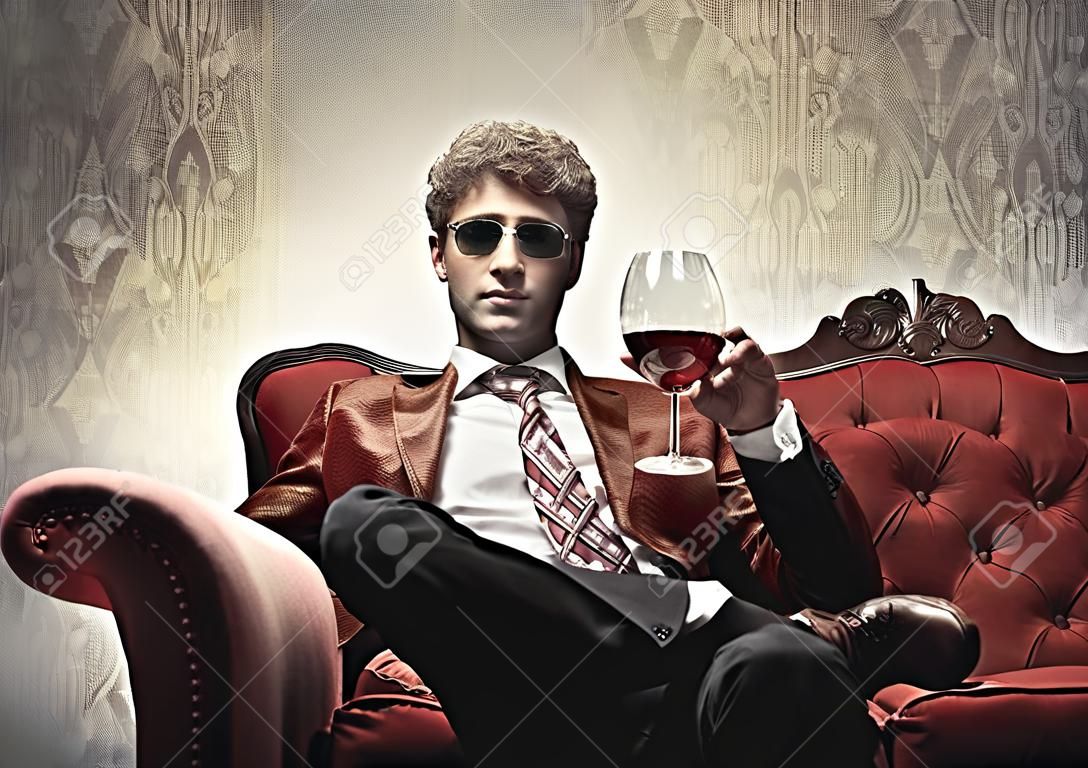 Elegante hombre sentado en un sofá de terciopelo y sosteniendo un vaso de vino