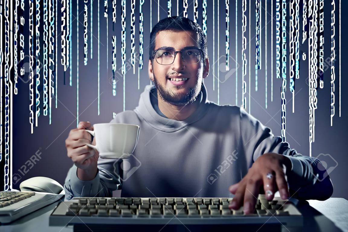 Sonriente a joven sentado frente a una pantalla de ordenador y la celebración de una taza de café