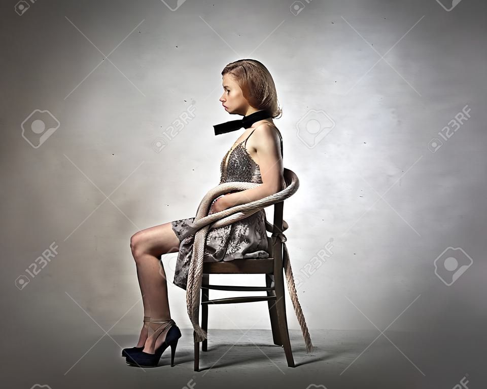Sad verängstigte junge Frau gefesselt an einem Stuhl fest