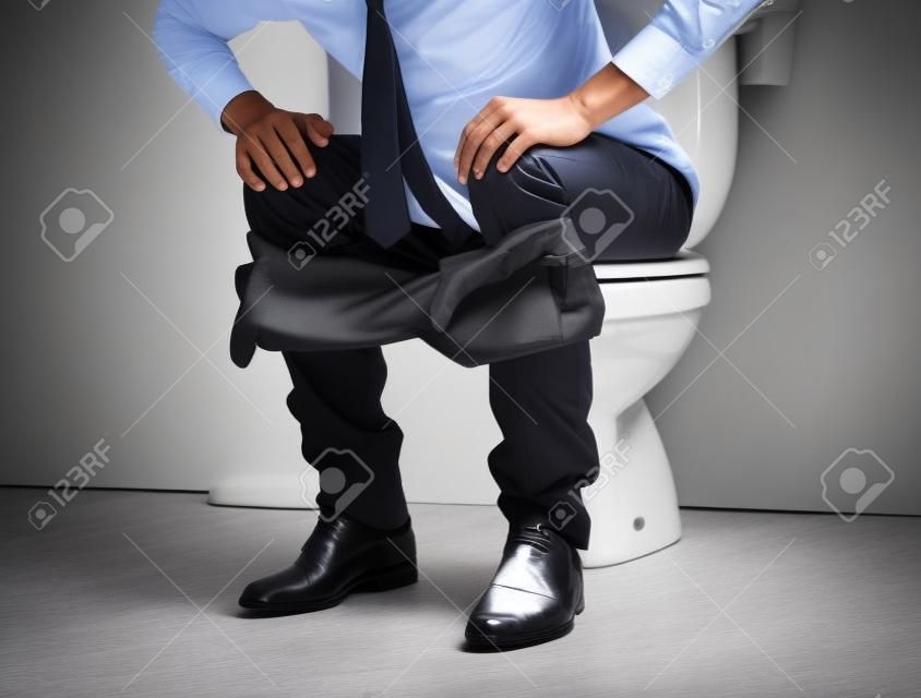 Młody biznesmen na toalecie kładzie ręce na kolanach