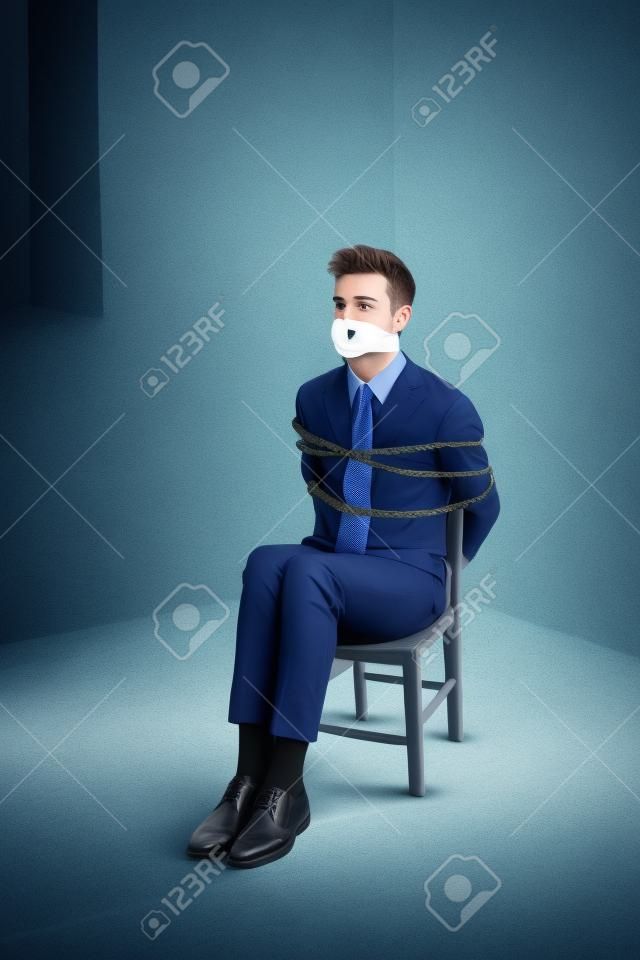 Hombre de negocios joven atado a una silla y amordazada en un sótano