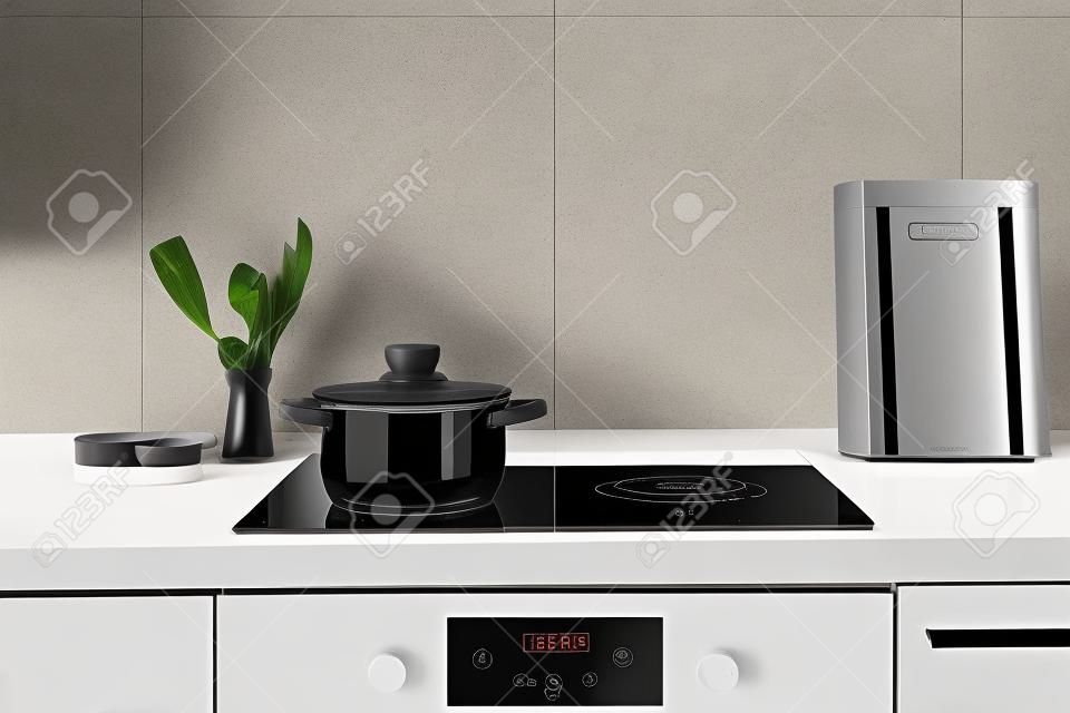 Czarna ceramiczna kuchenka indukcyjna z zegarem na panelu sterowania i rondelkiem na górze. Współczesny dom z nowoczesnym wnętrzem, wbudowanym sprzętem kuchennym i białą płytką na ścianie z miejscem na kopię
