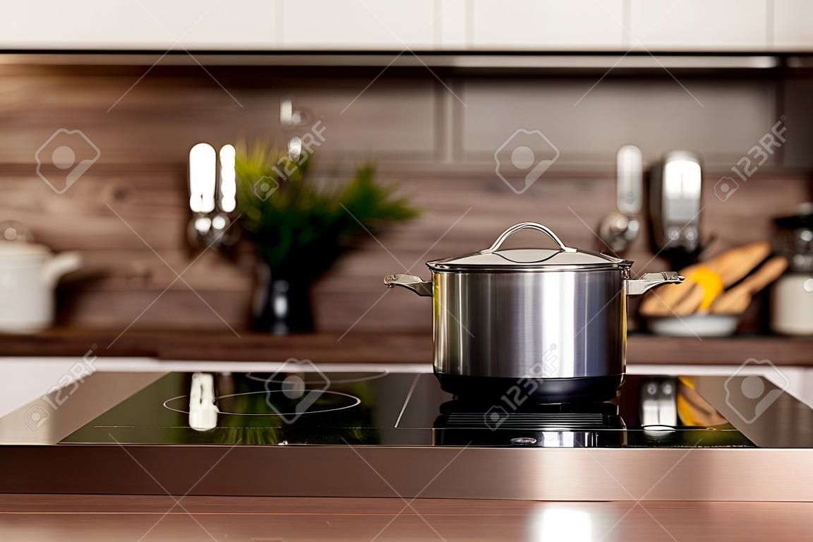 Mise au point sélective sur une marmite sur une cuisinière électrique près d'un comptoir en bois sur fond flou avec des placards de cuisine blancs dans un intérieur moderne. Cuisine et concept de cuisine maison