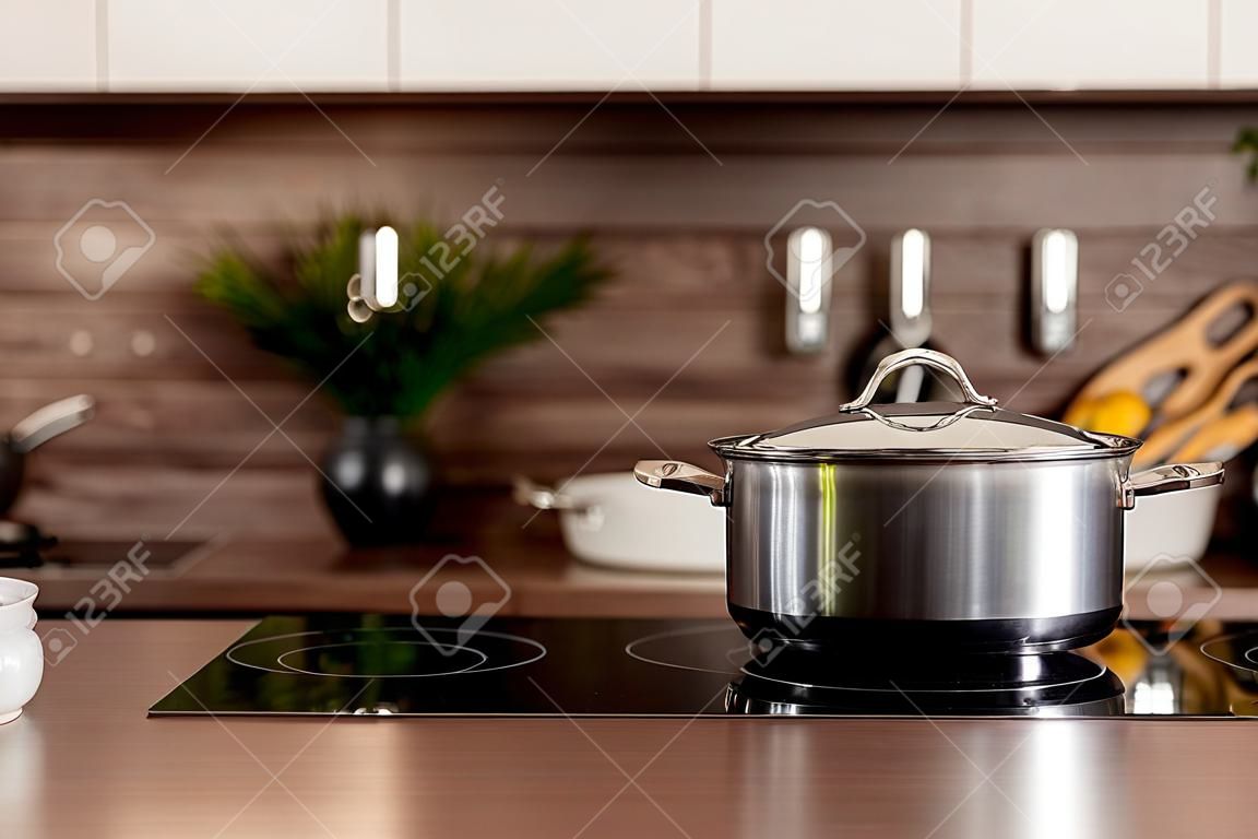 Selectieve focus op kookpot op elektrisch fornuis in de buurt van houten aanrecht tegen wazige achtergrond met witte keukenkasten in modern interieur.