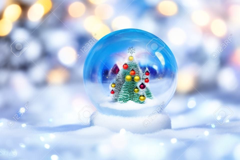 Glass globe in snow with Christmas decoration and colorful background. Christmas glass ball. Selective focus.