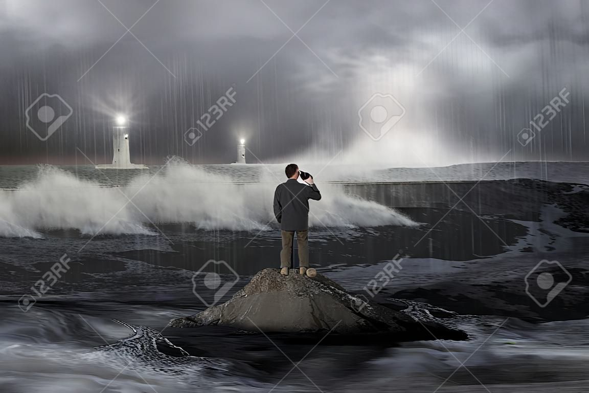 Del hombre en roca mirando al faro en el mar con la tormenta, el trueno, alijo y las olas en la oscuridad