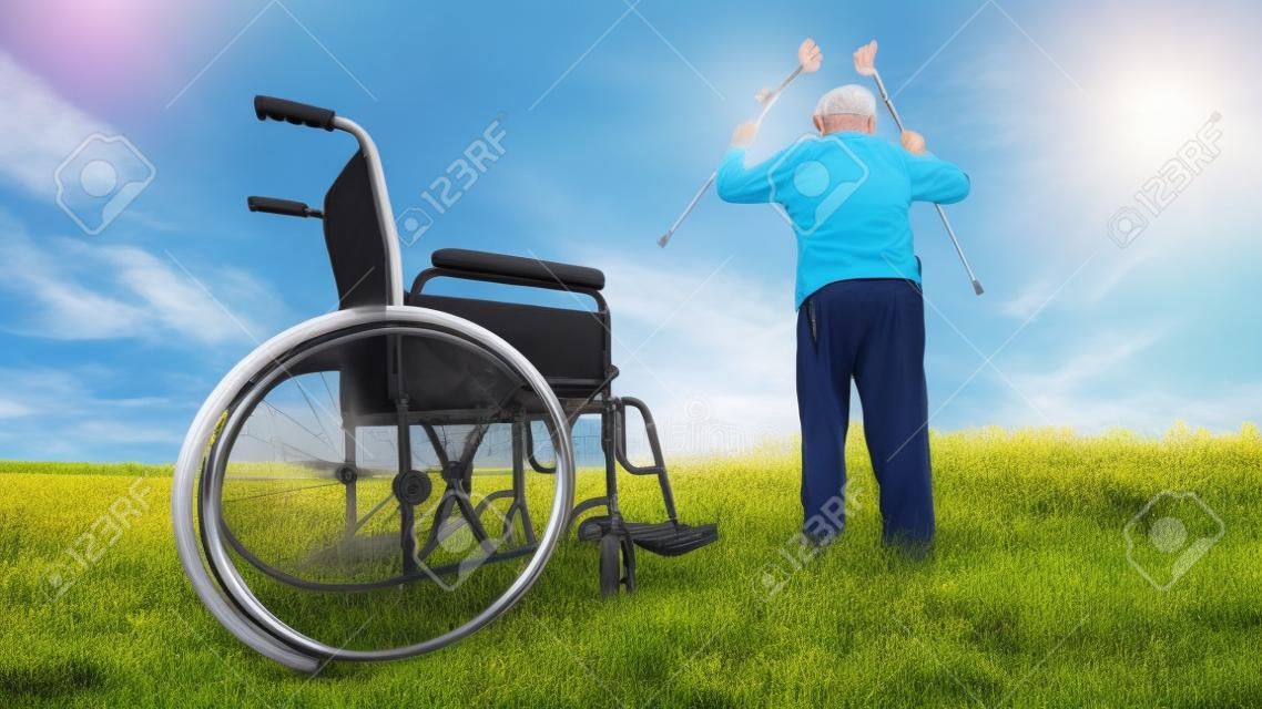 la recuperación milagro: El viejo hombre se levanta de la silla de ruedas y levanta las manos en alto. Rodada en un prado. concepto de recuperación