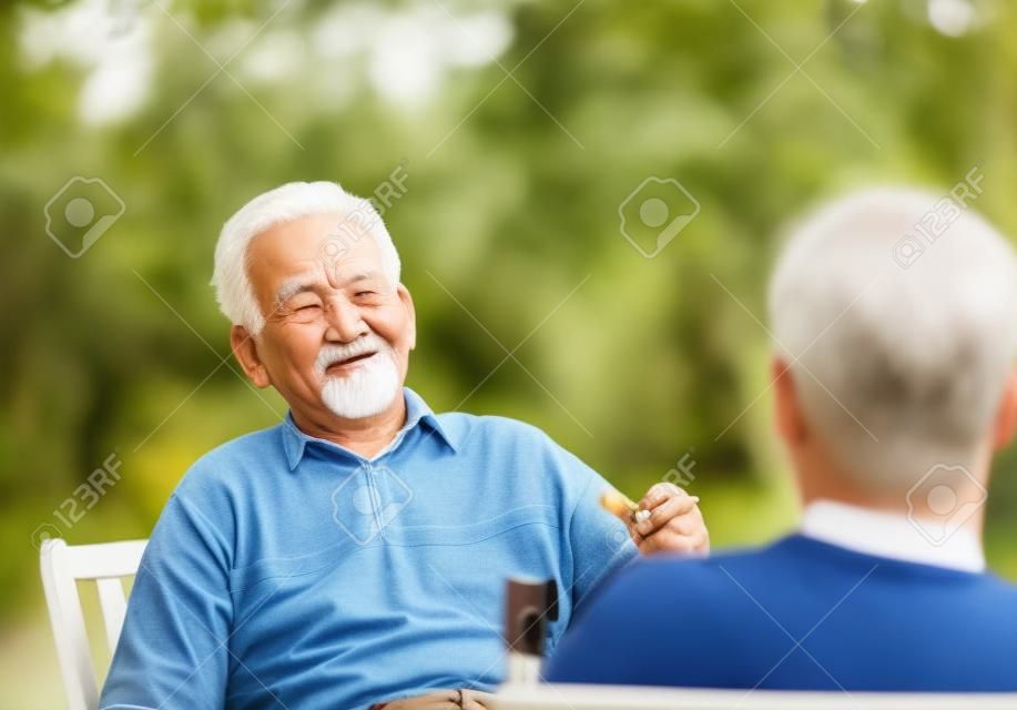 Viejo hombre con el cigarrillo en la mano en el chat con el nieto en el jardín