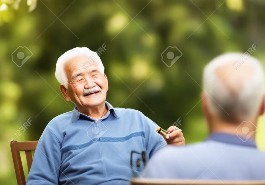Viejo hombre con el cigarrillo en la mano en el chat con el nieto en el jardín