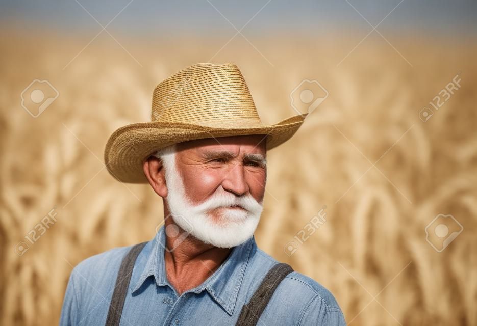 Portrait of old farmer with white beard in overall and with straw hat in corn field