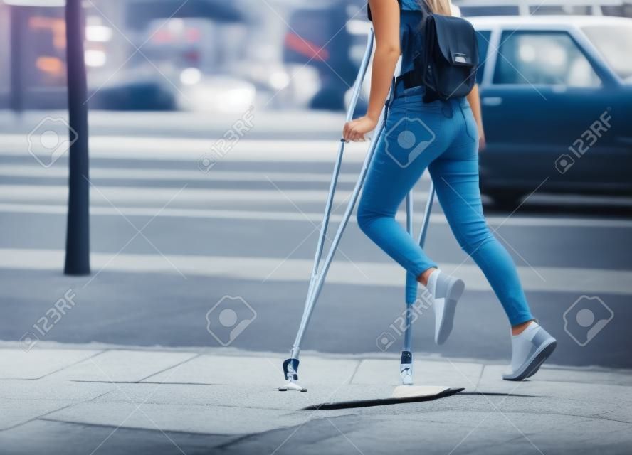 Bella ragazza che cammina con le stampelle con la gamba piegata in strada