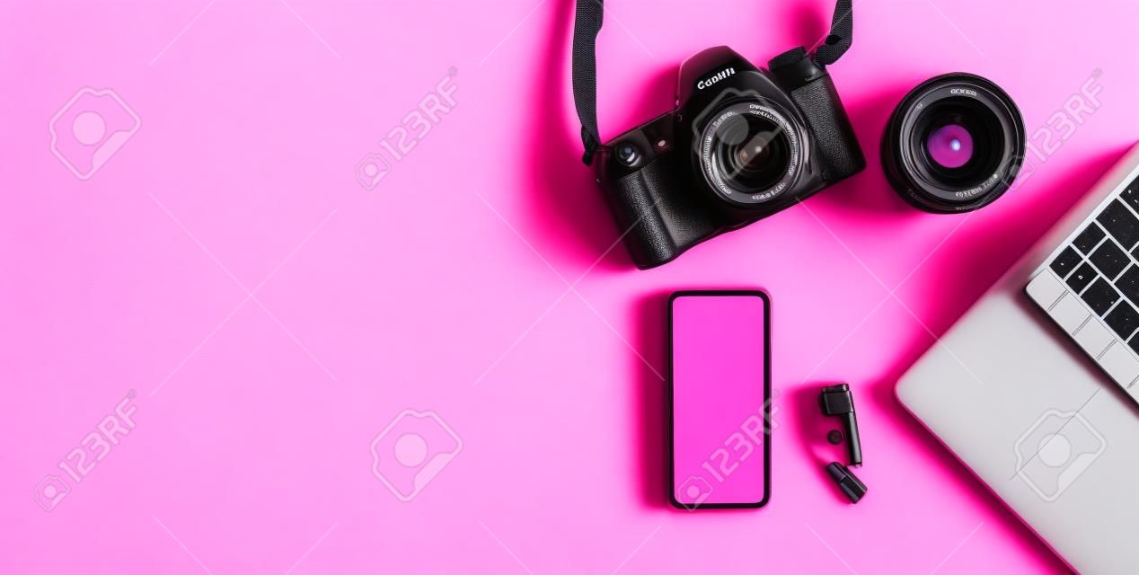 Kamera, objektiv, laptop und smartphone mit leerem weißem display auf rosa hintergrund. arbeitsplatz des fotografen. flach legen, kopieren.