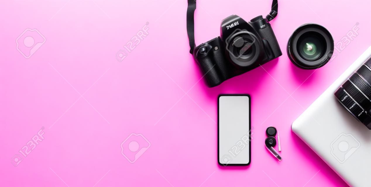 Kamera, objektiv, laptop und smartphone mit leerem weißem display auf rosa hintergrund. arbeitsplatz des fotografen. flach legen, kopieren.