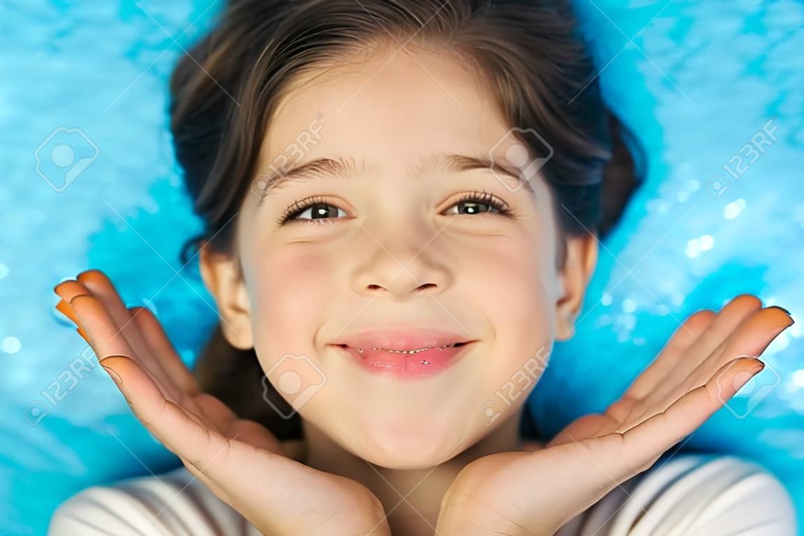 Portret szczęśliwej podekscytowanej dziewczyny z otwartymi ustami trzymającej ręce na jej twarzy odizolowanej na niebieskim tle