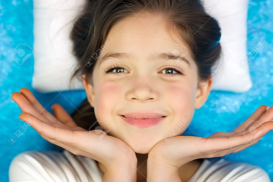 Portret szczęśliwej podekscytowanej dziewczyny z otwartymi ustami trzymającej ręce na jej twarzy odizolowanej na niebieskim tle