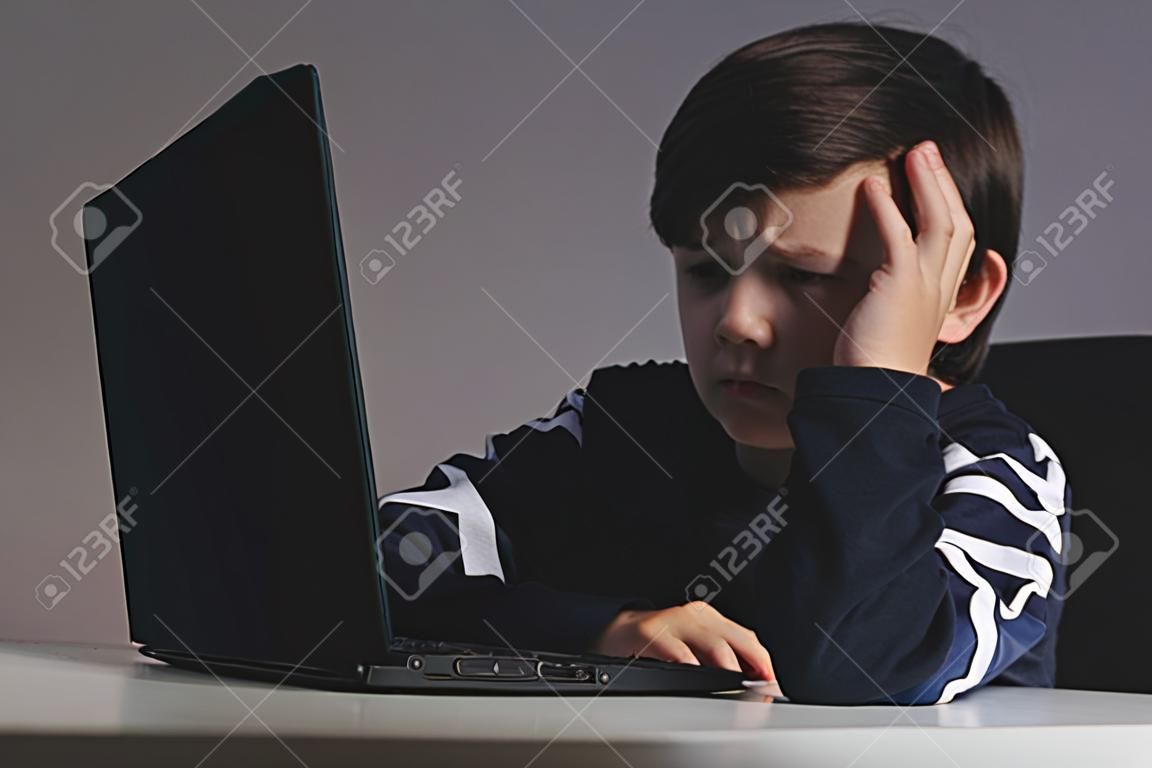 Nahaufnahmebild des Mobbings des jugendlichen Jungen, der sich vor dem Computer verärgert fühlt. Gestresster trauriger Junge schikaniert von seinen Mitschülern.