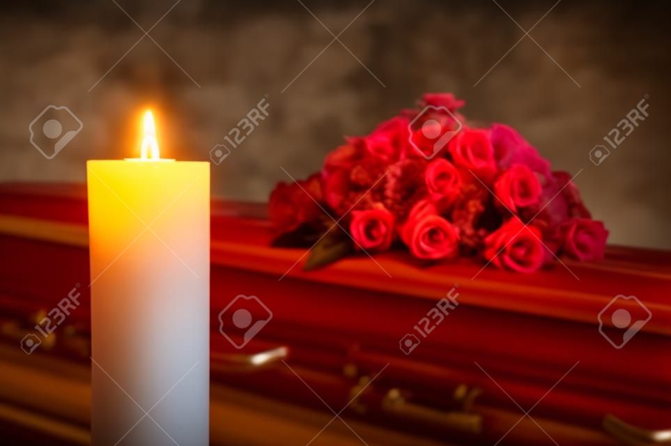 A burning candle with a coffin and a flower arrangement on the background in a mortuary