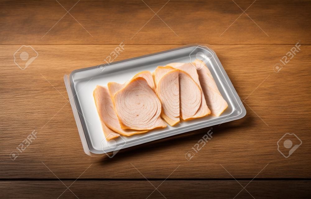 Thin sliced smoked turkey slices in a plastic tray on a table illuminated with natural light.