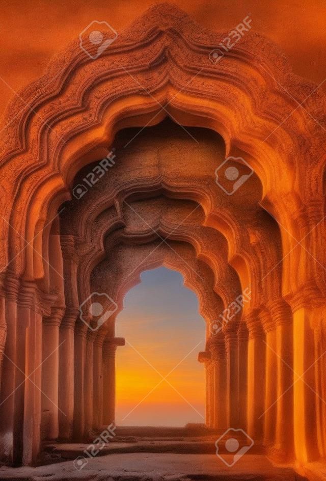 インドの日没での古代寺院の古い台無しにされたアーチ